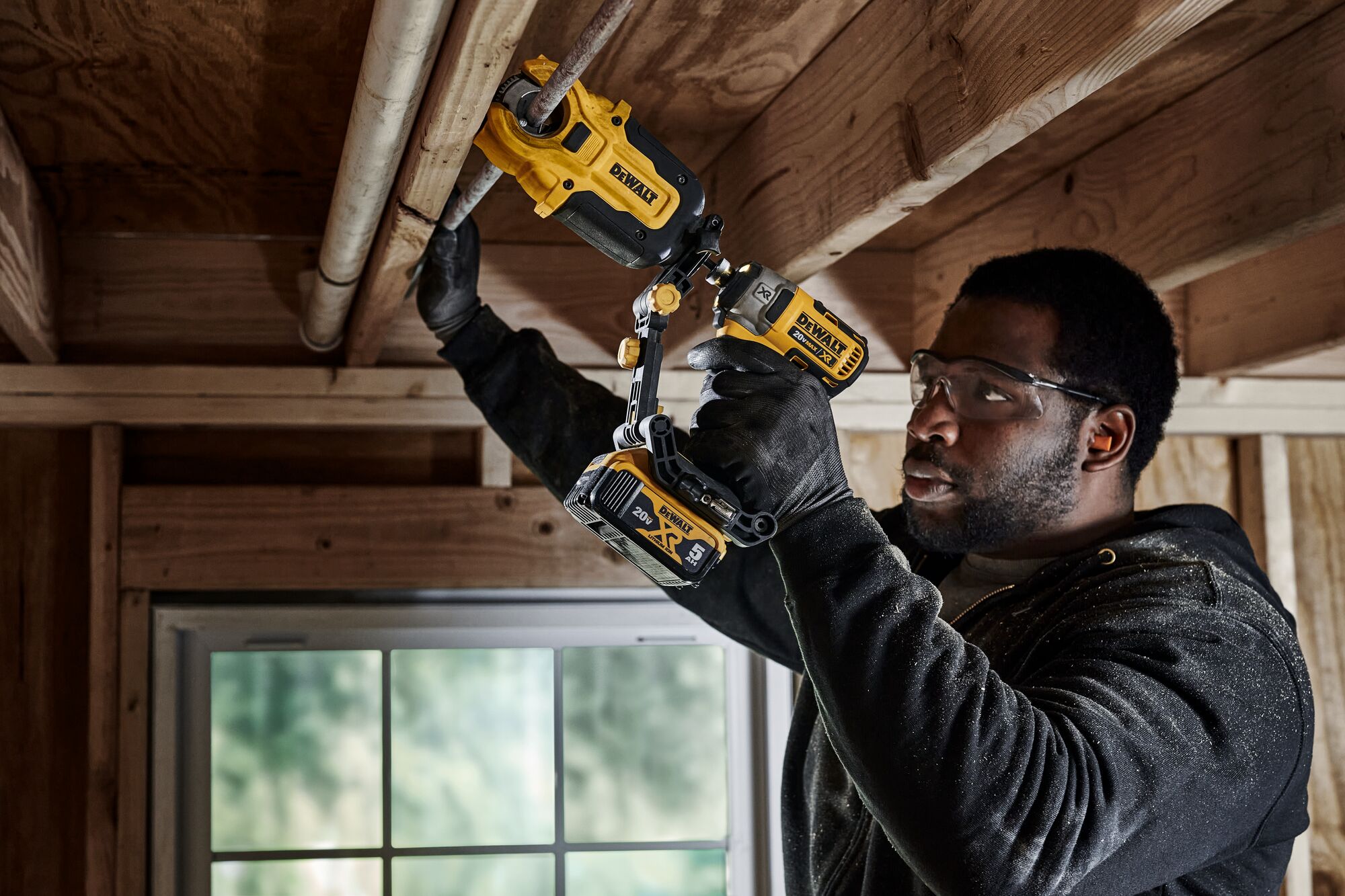 End user using DEWALT IMPACT CONNECT Copper Cutter attachment on Impact Driver to cut copper pipe running along board above his head.
