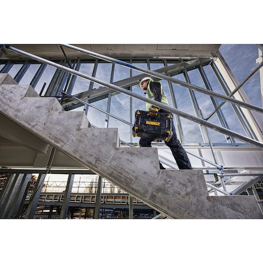 T stak portable Bluetooth radio and charger being carried up stairs by a worker.